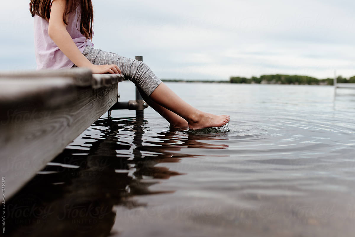 Anonymous girl sitting on a dock dipping feet into a calm lake
