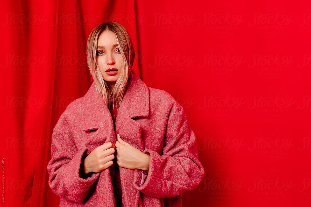Young woman standing in oversized coat near red curtain