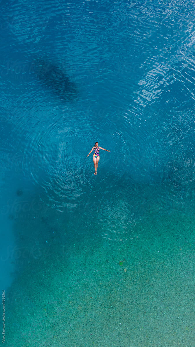 young woman floating in turquoise sea water, drone overhead