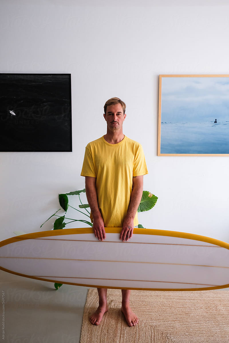 Portrait of a surfer holding his surfboard inside his minimalist loft