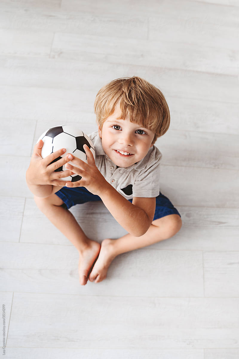 Cute young boy holding a ball in his hands looking at the camera and smiling