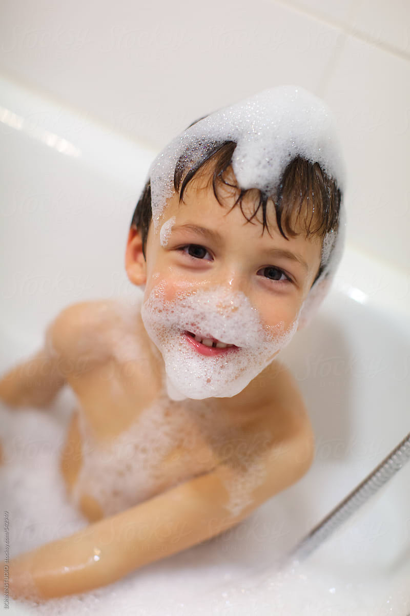 Young boy bathing with soap bubbles in the bathtub.