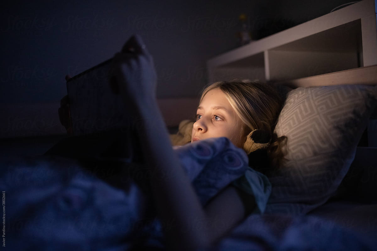 little girl lying in bed watching a movie