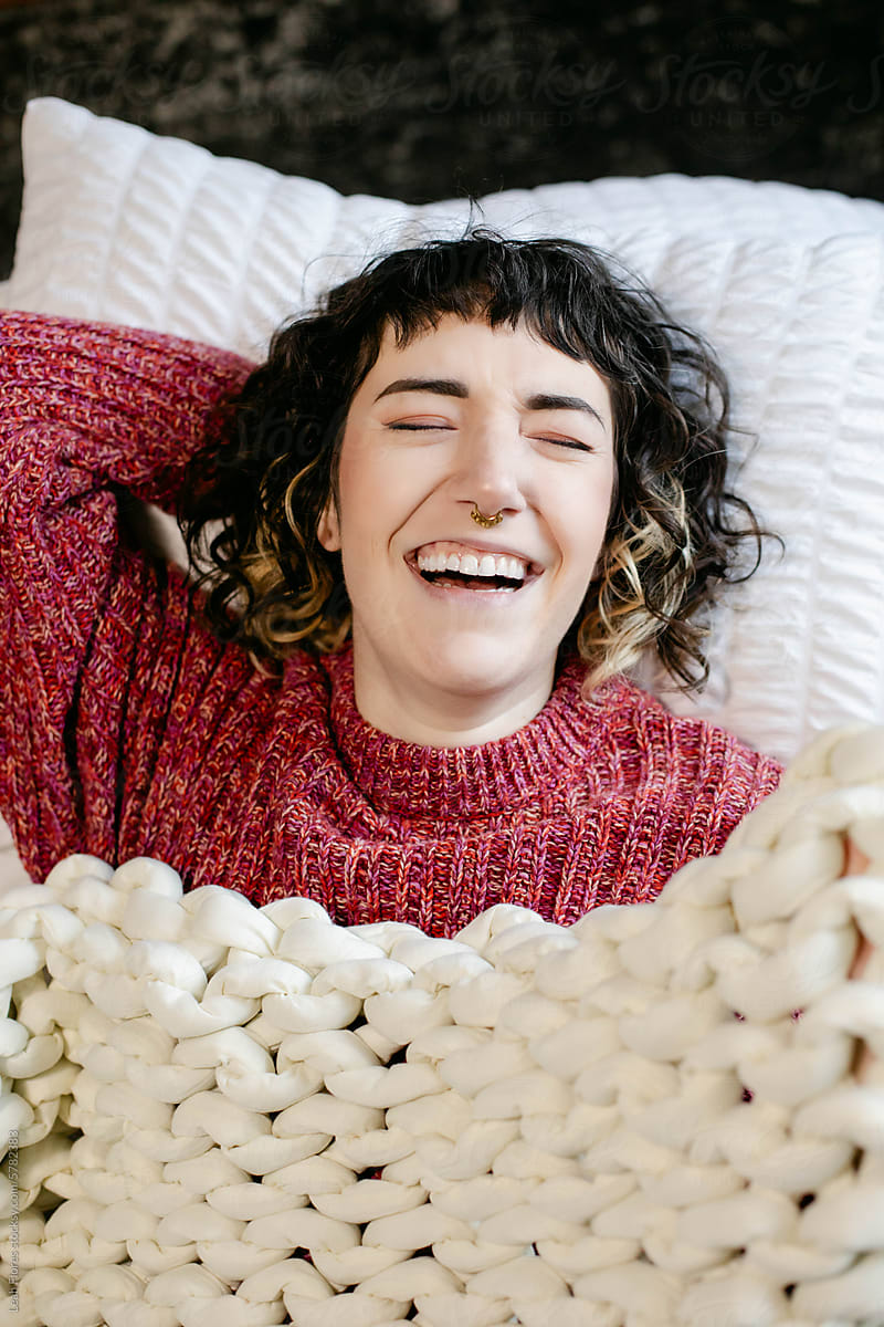 Laughing Woman on Bed under Knit Blanket