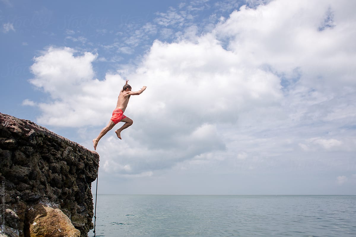 Summer fun - man jumping off cliff into the ocean