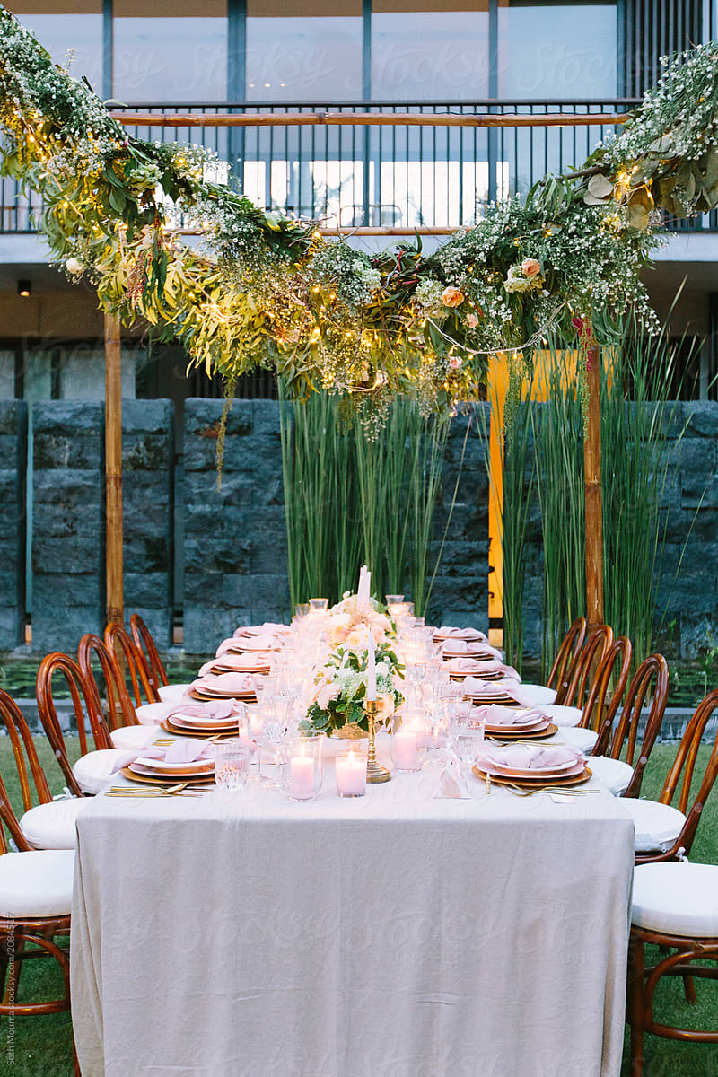Outdoor, tropical wedding reception table with hanging greenery garlands at dusk