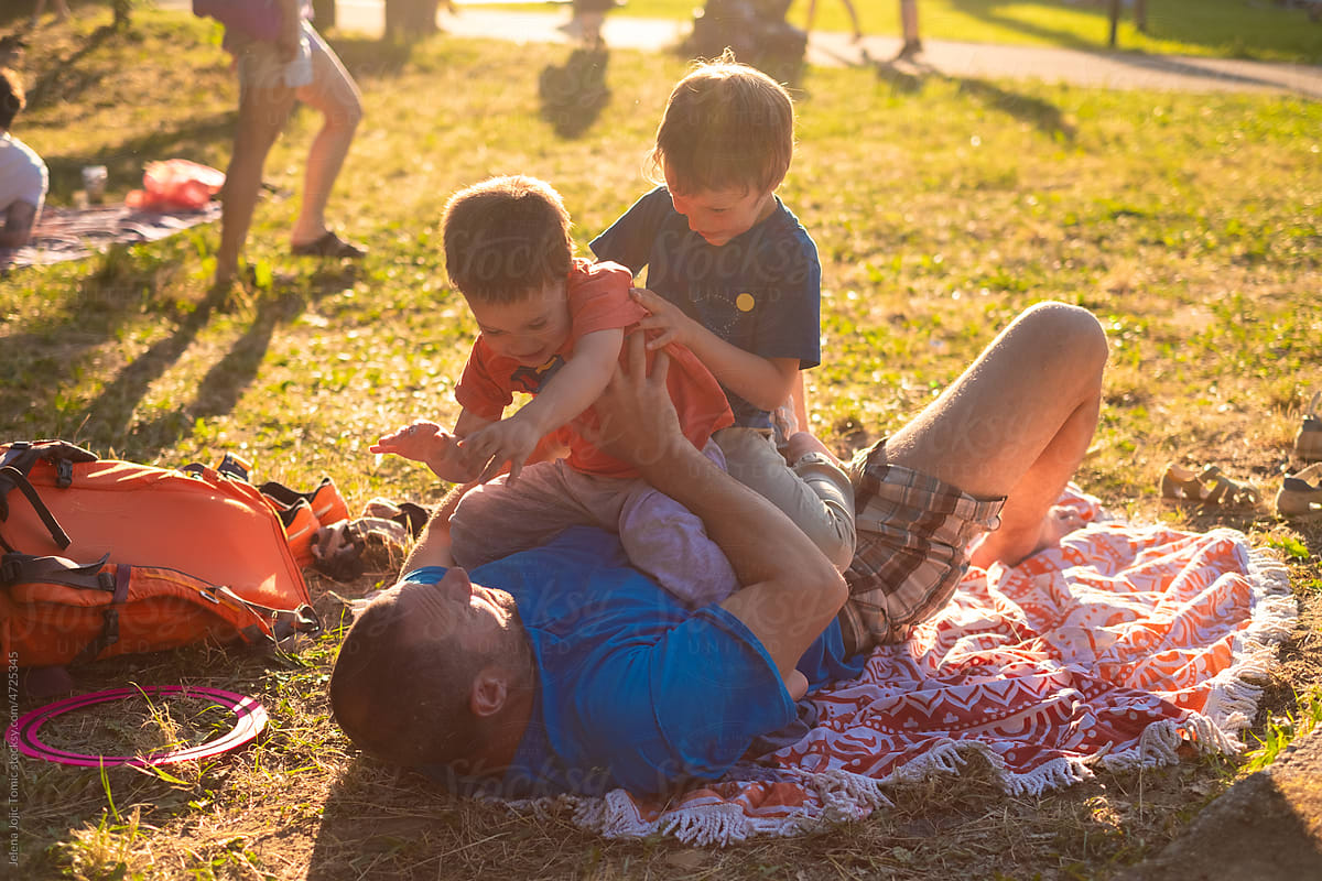Kids play, wrestle, climb and annoy their father outdoors in a park