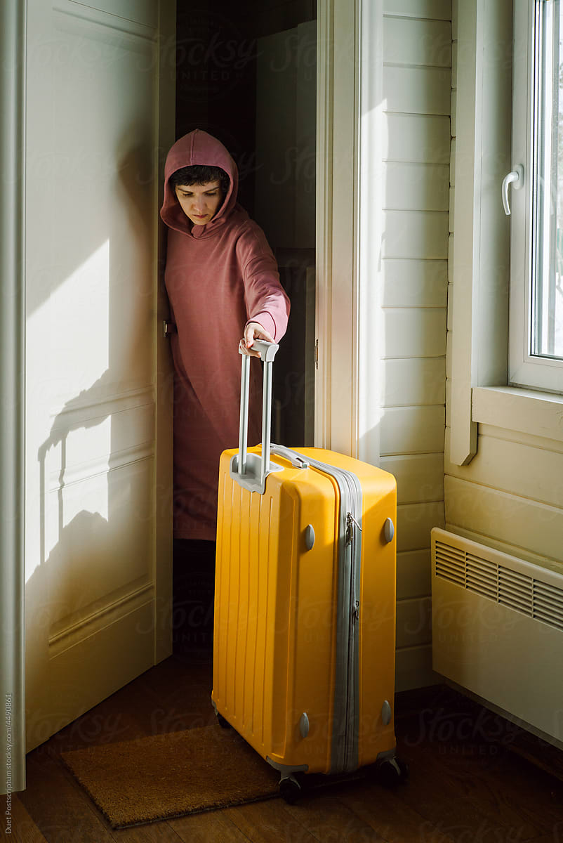 Young woman rolls out a large yellow plastic travel suitcase