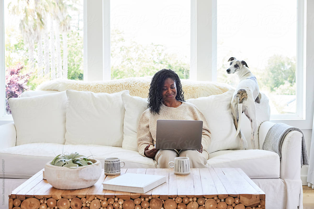 Mature Black woman on computer at home on sofa with her pet dog