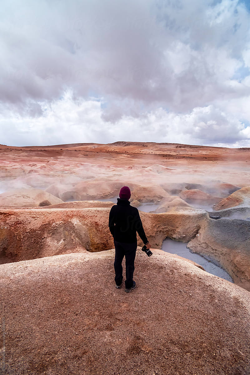 Photographer in front of some geysers with volcanic activity and mud pits
