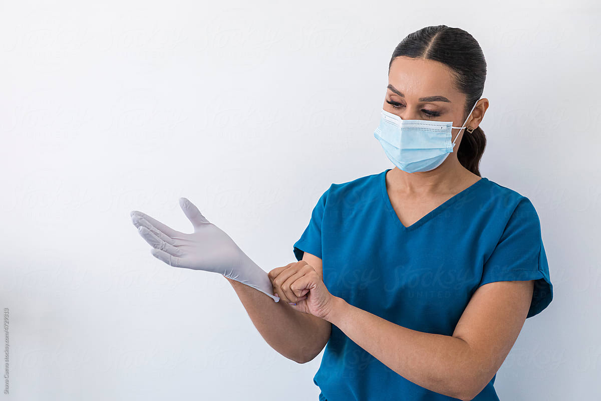 A dentist putting on gloves in front of a white wall
