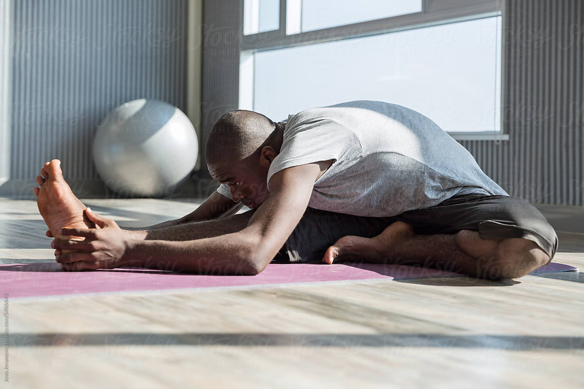 Man practicing janusirsasana yoga pose with one knee bent out to side