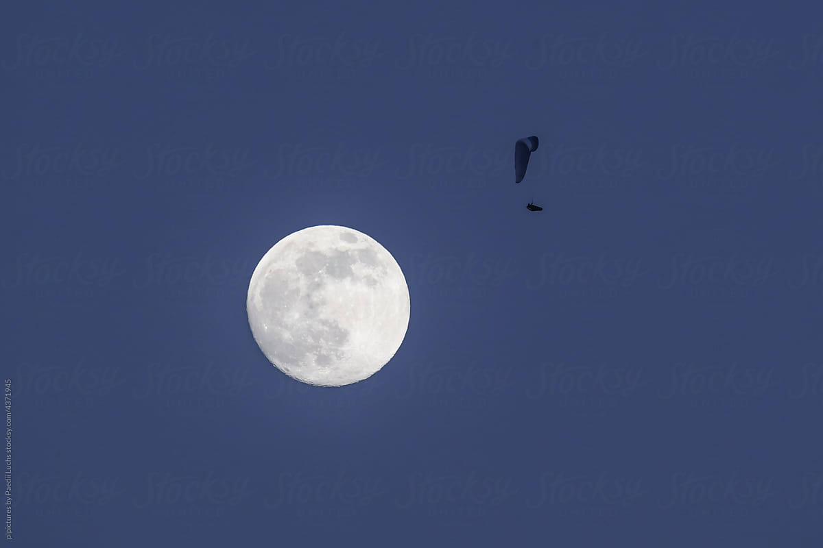Paraglider flying next to full moon.