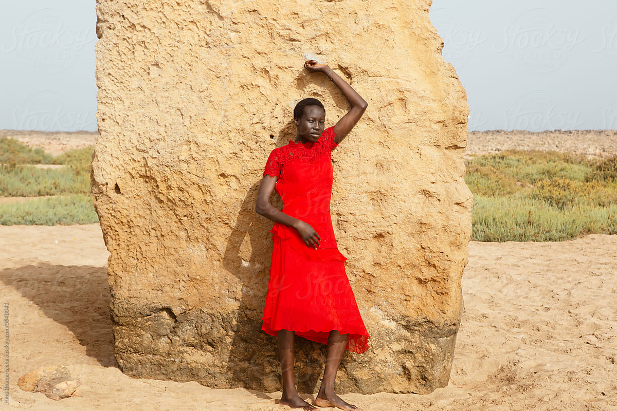 portrait of a young woman of color in a flowing red dress at the beach