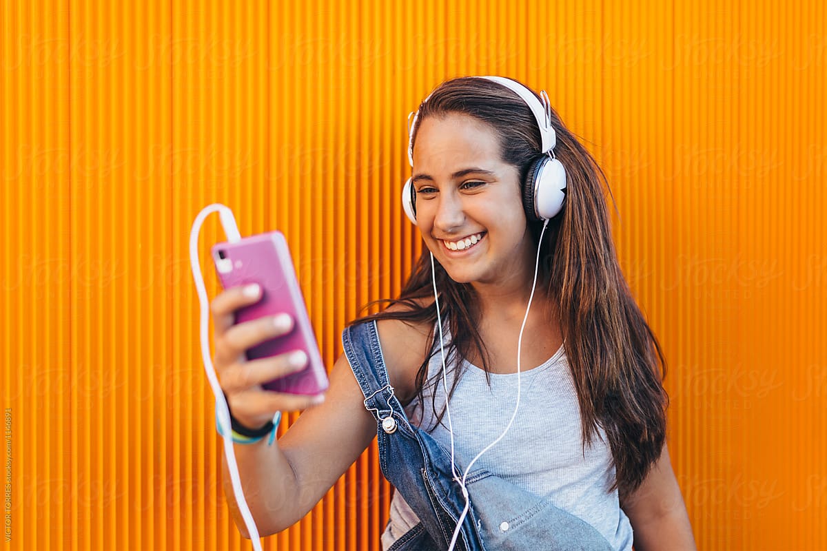 Happy Teen Girl Using A Smartphone And Headphones by Stocksy