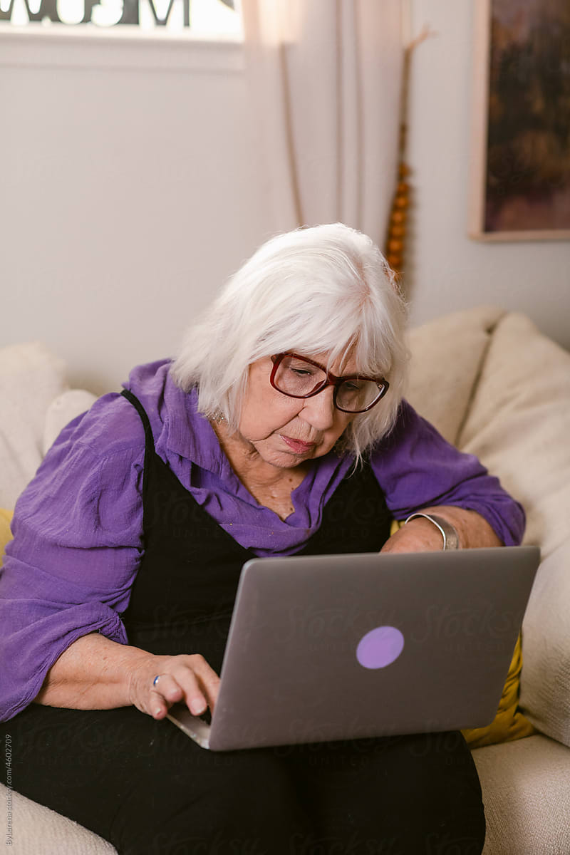 Elderly woman using laptop on sofa at home