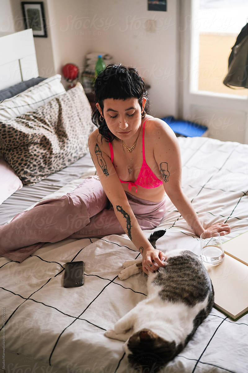 Informal woman stroking cute cat on bed