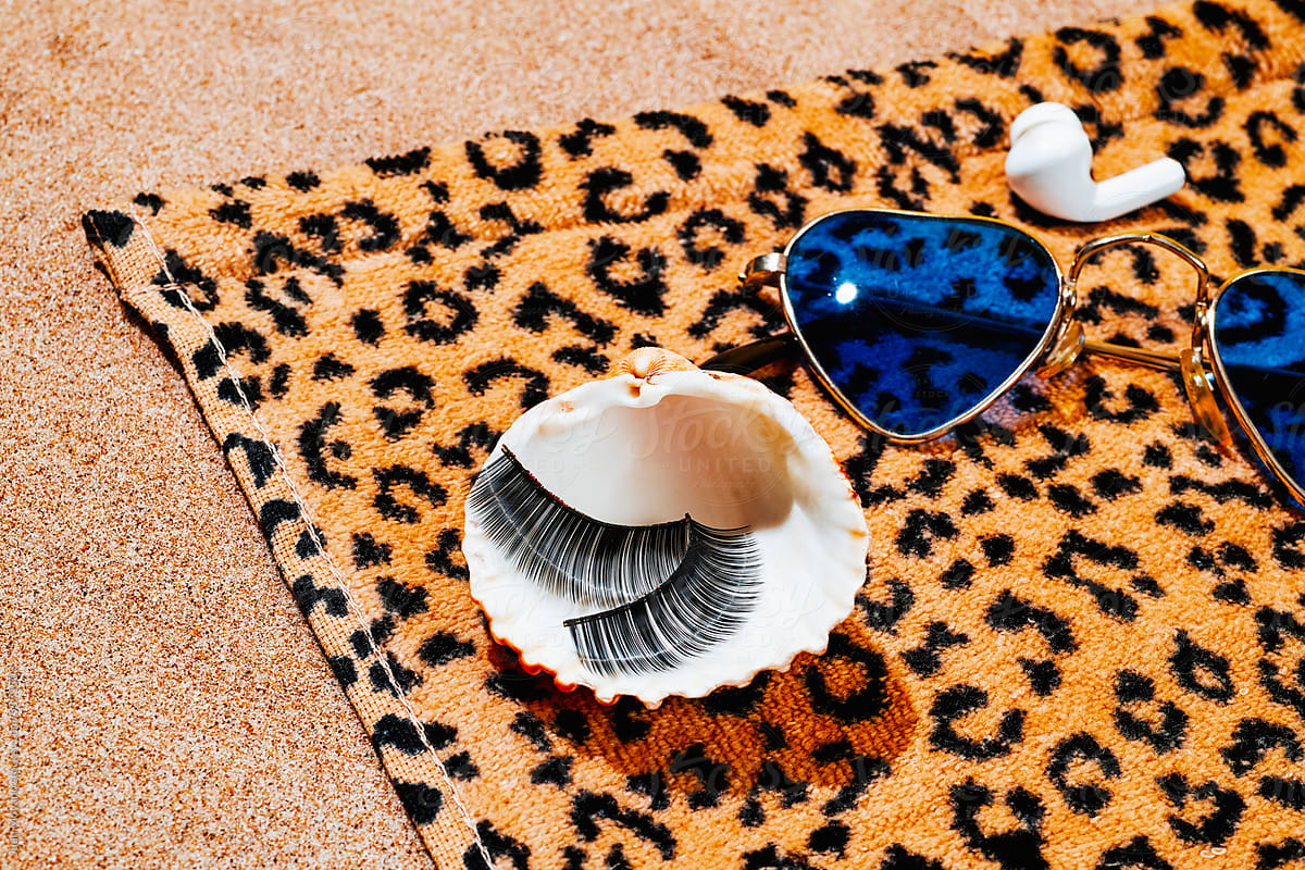 fake eylashes, seashell and sunglasses on a beach towel