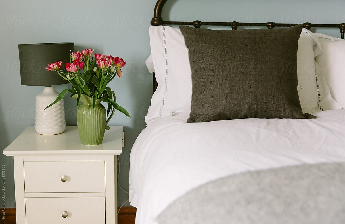 A vase of tulips next to a bed.