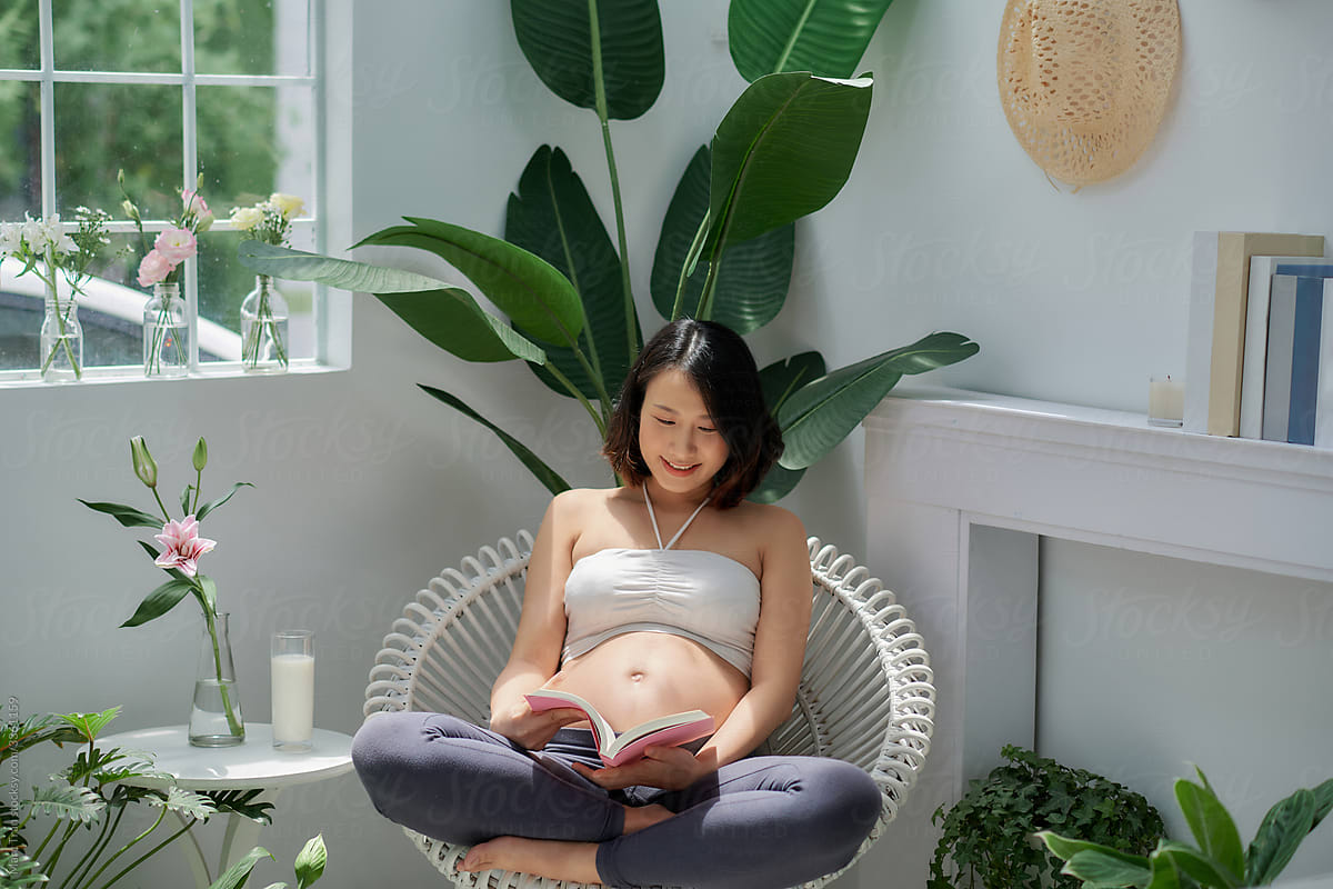 Pregnant young woman on the armchair and reading a book