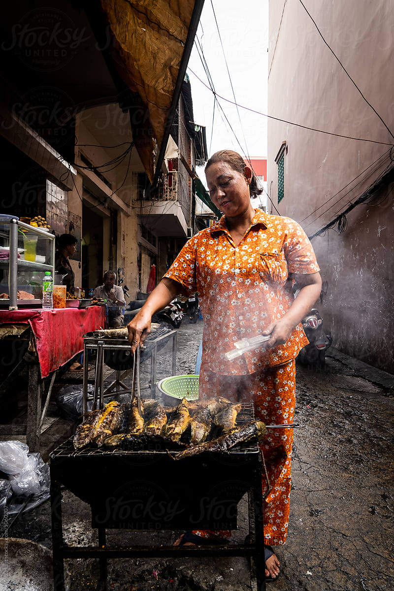 Phnom Penh street food seller cooks catfish on a grill