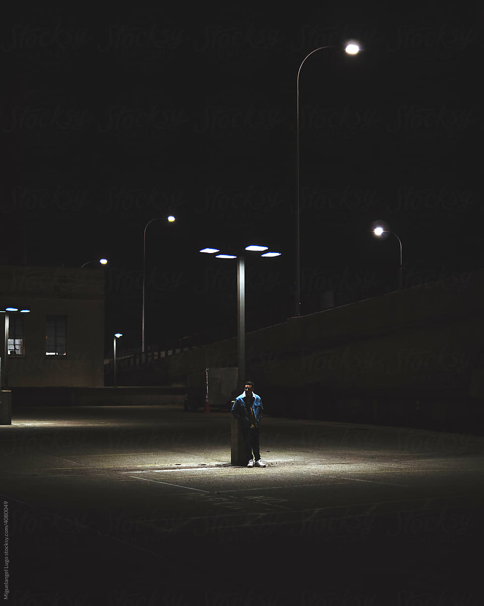 Young Man Under Light Post in a Dark Moody Parking Lot