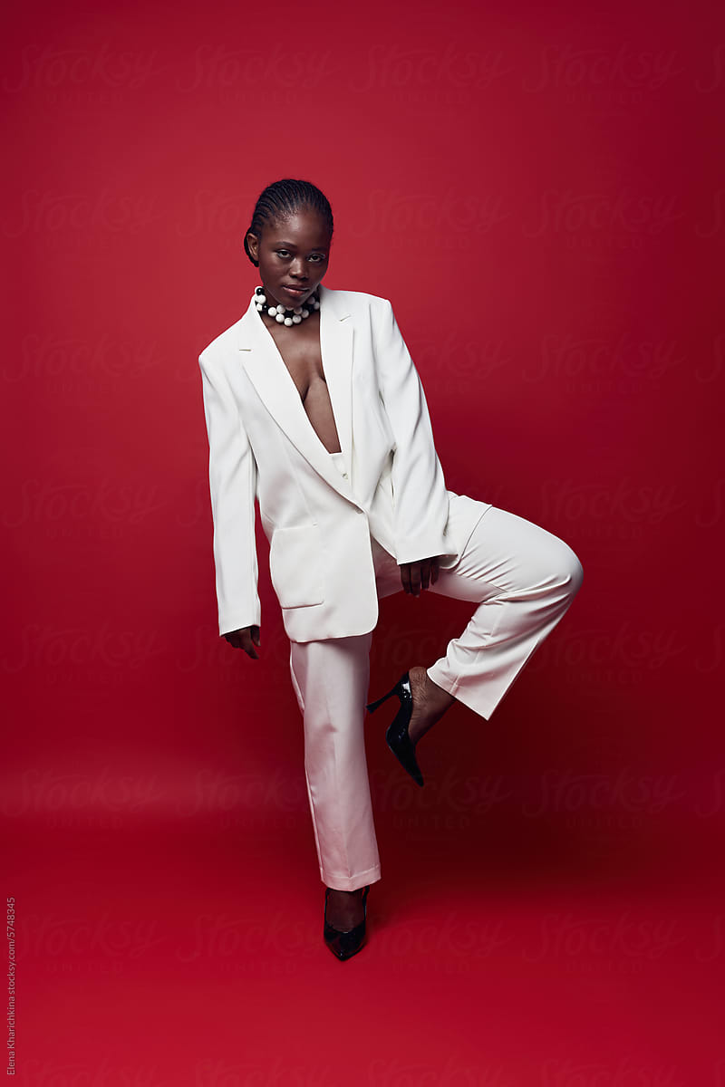 Fashionable black model in white suit posing on red background