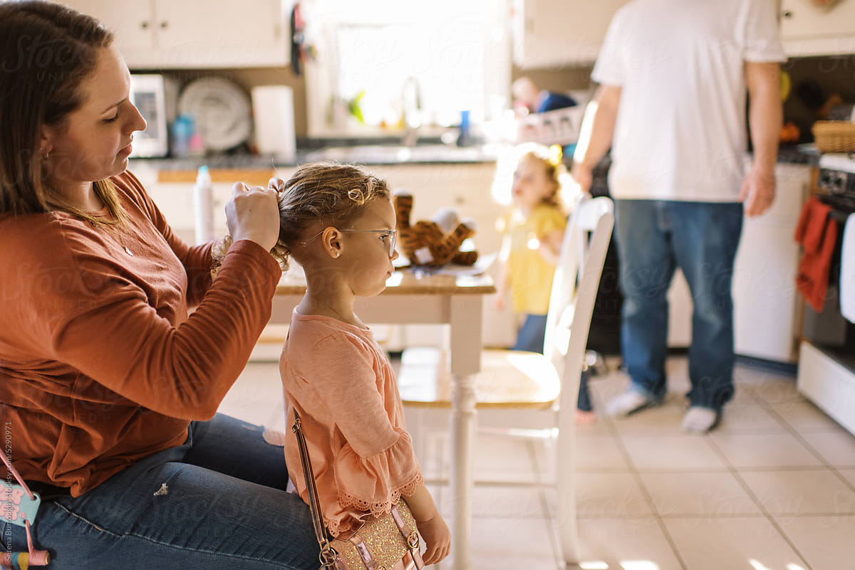 Mom styling hair of her toddler daughter in kitchen at home
