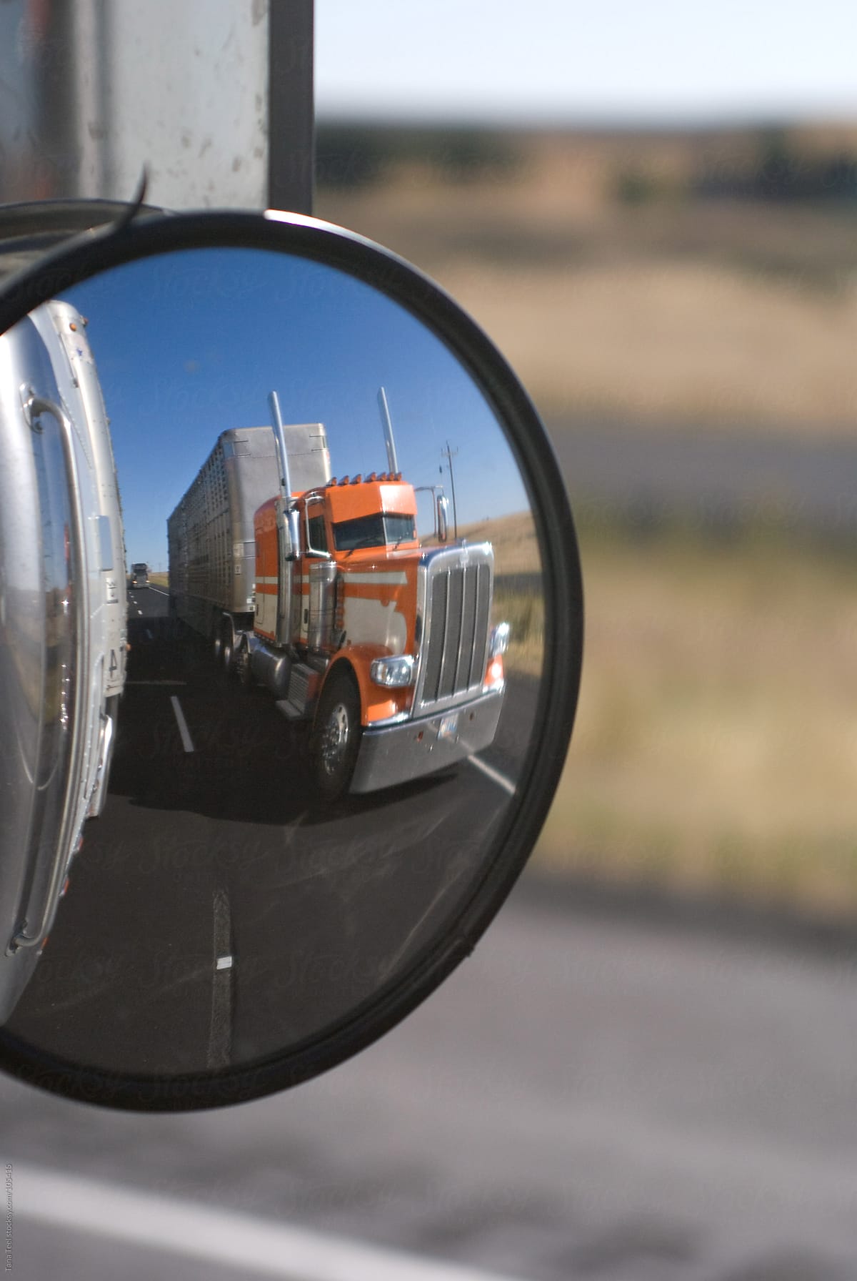 A passing truck in another truck\'s side mirror