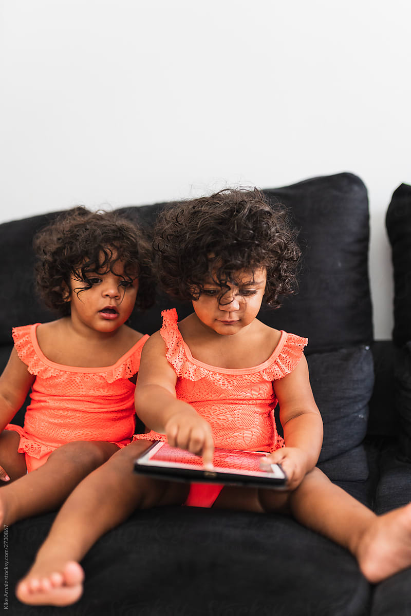 one years old twins playing with an tablet on the couch