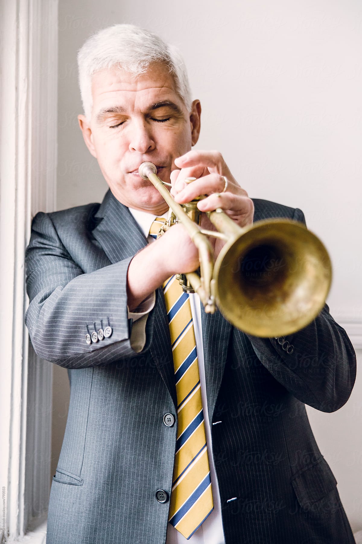 silver haired man with eyes closed blowing into trumpet