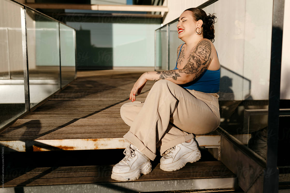 Positive tattooed woman sitting on stairs in summer