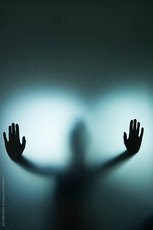 Backlit figure with hands pressed against frosted glass.