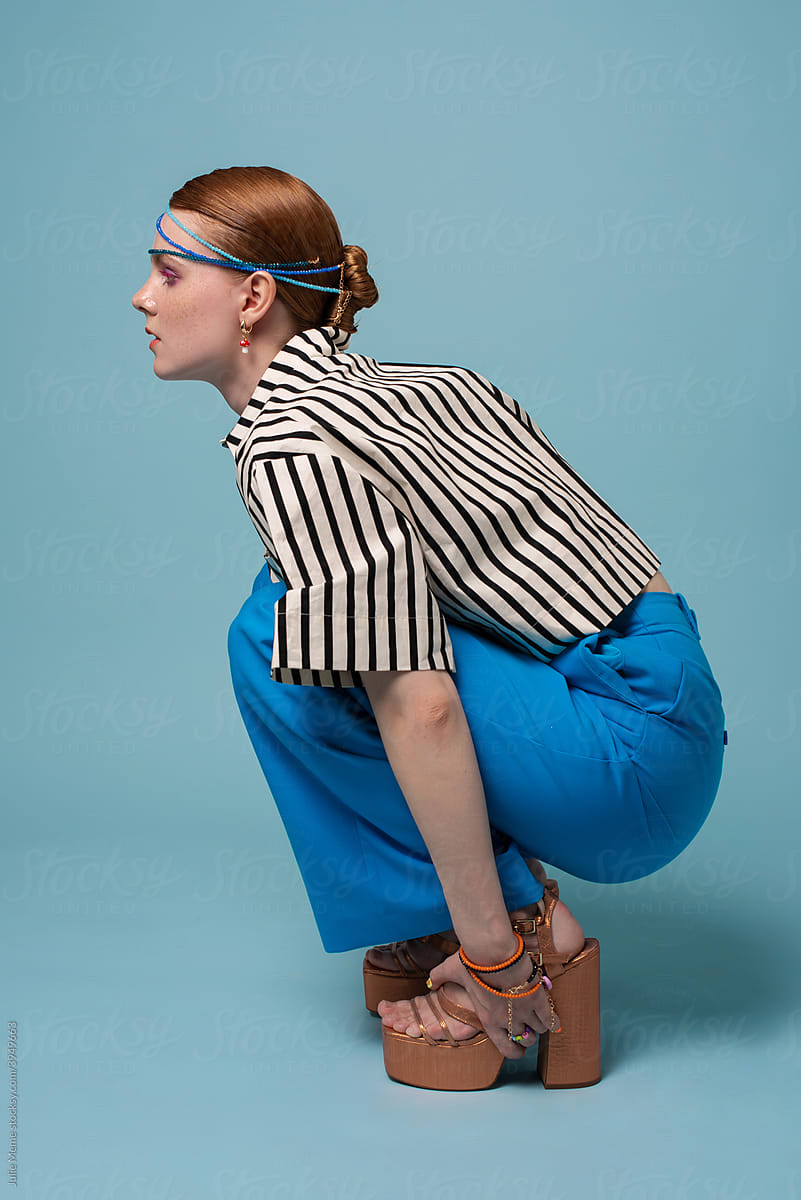 A girl sits in a striped shirt and blue trousers