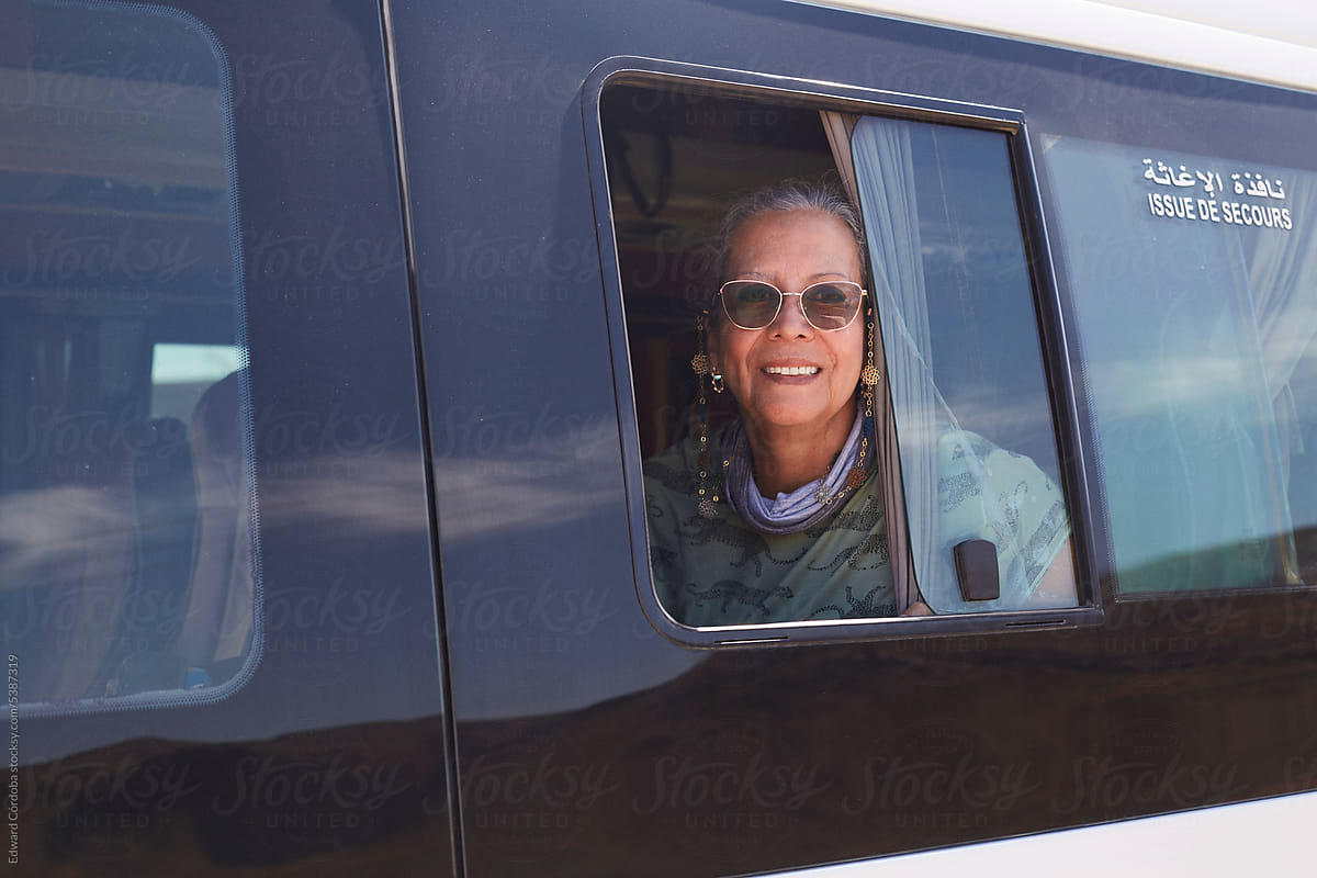 Mature woman with grey hair is sitting inside the van and looking out