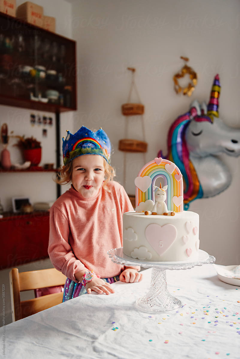 Girl with unicorn and pastel rainbow themed bday cake at home party