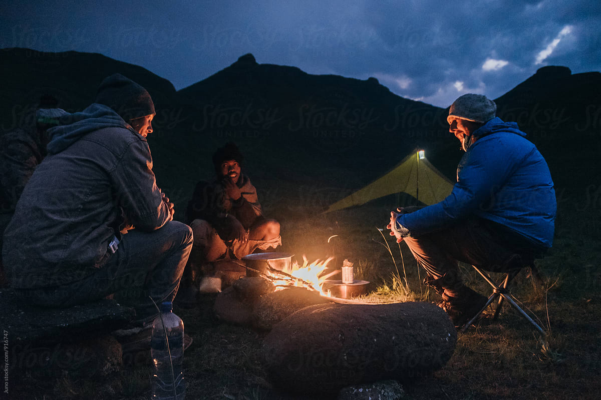 hiker outdoorsmen sitting around a camp fire at night