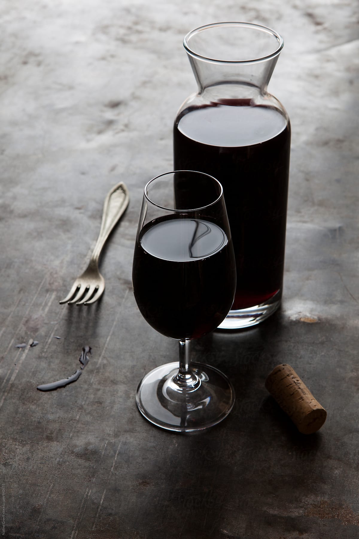 Wine carafe with glass of red wine, spills, fork and a cork