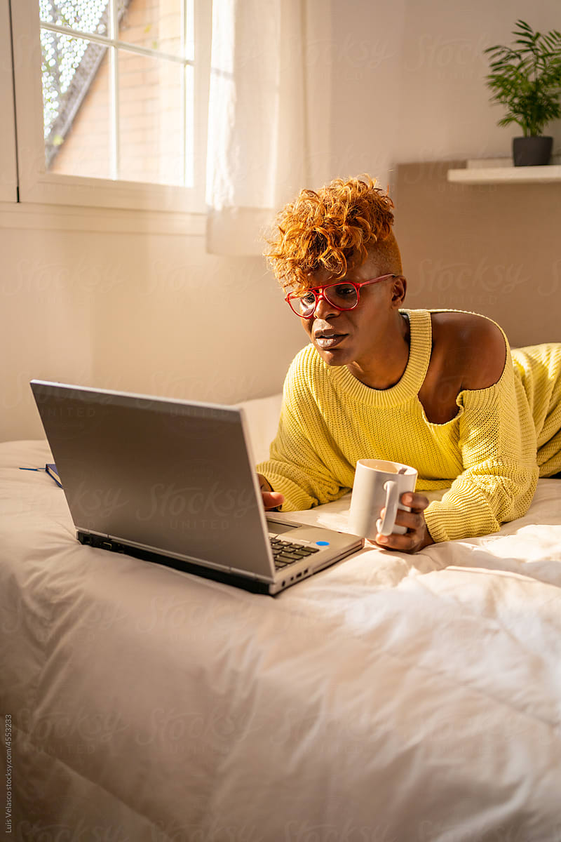 Black Woman With Laptop Having A Coffee Laying On The Bed.