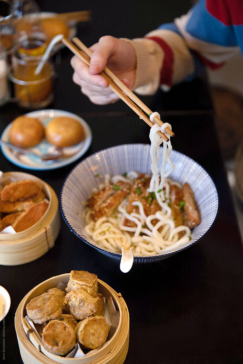 Male hand picking up noodles using chopsticks for eating