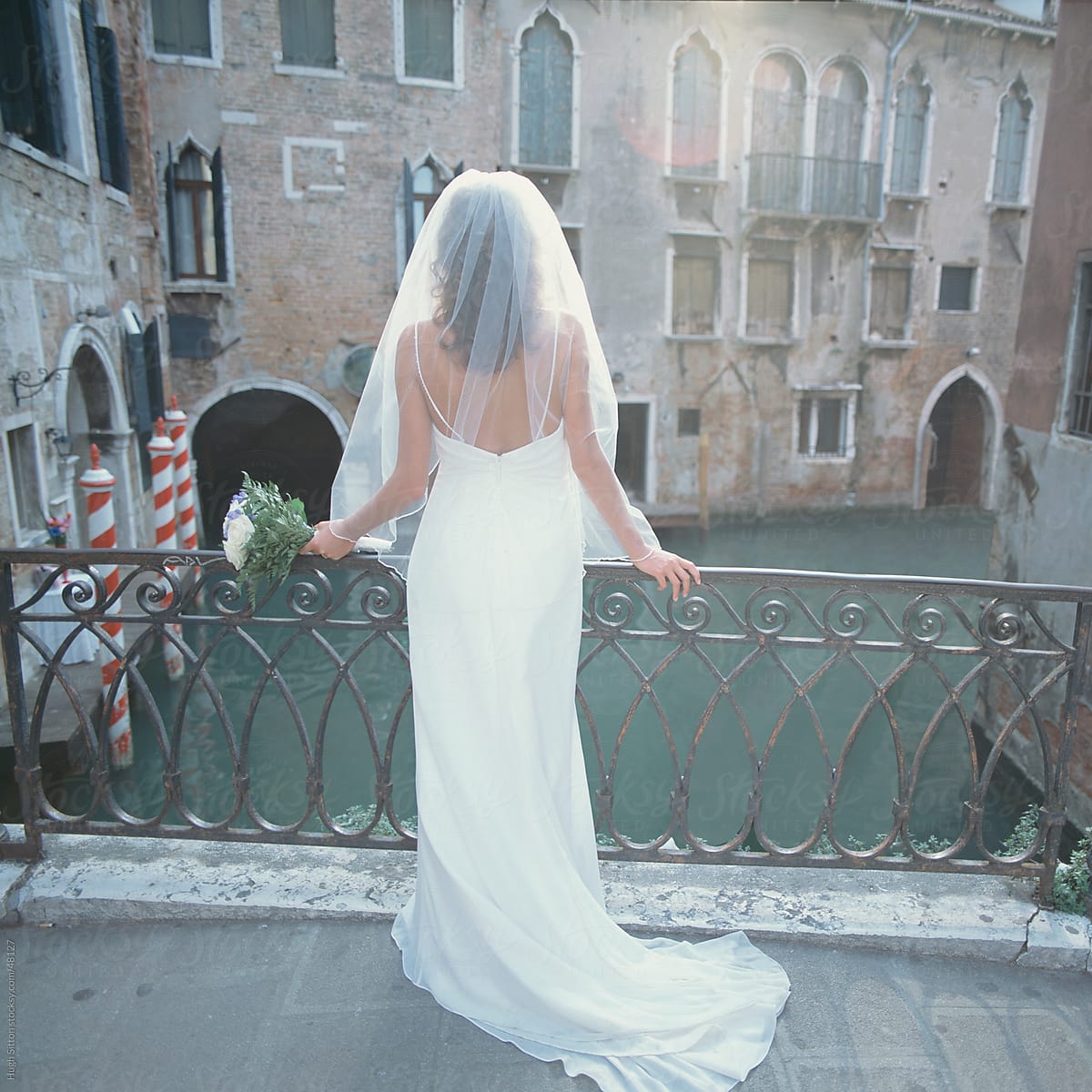 Bride in wedding dress on bridge overlooking canal. Venice. Italy.