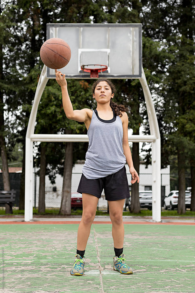 A full-body portrait of a female athlete spinning a basketball