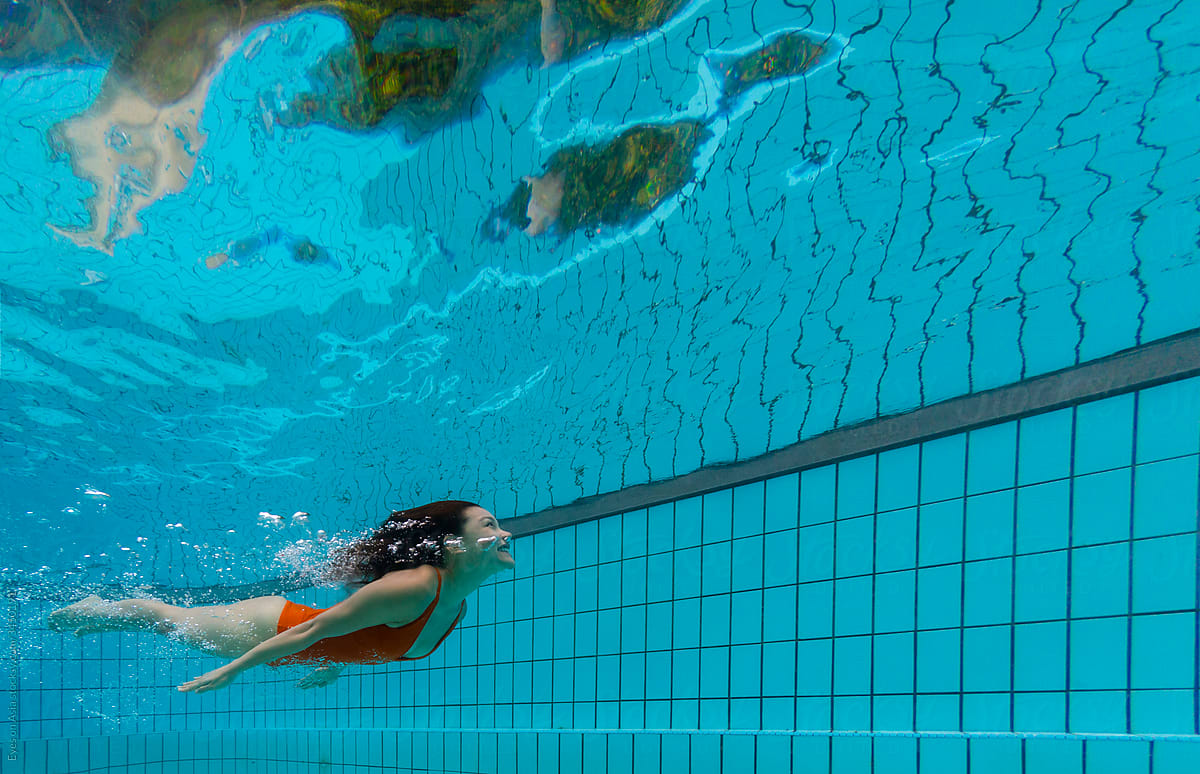 A woman in a red swimsuit is diving underwater in a pool while looking up