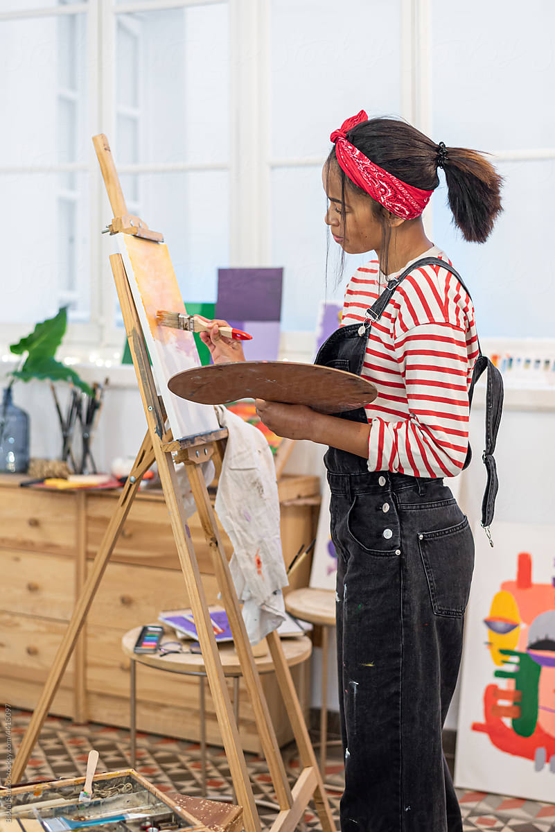 Black woman painting on easel in art studio