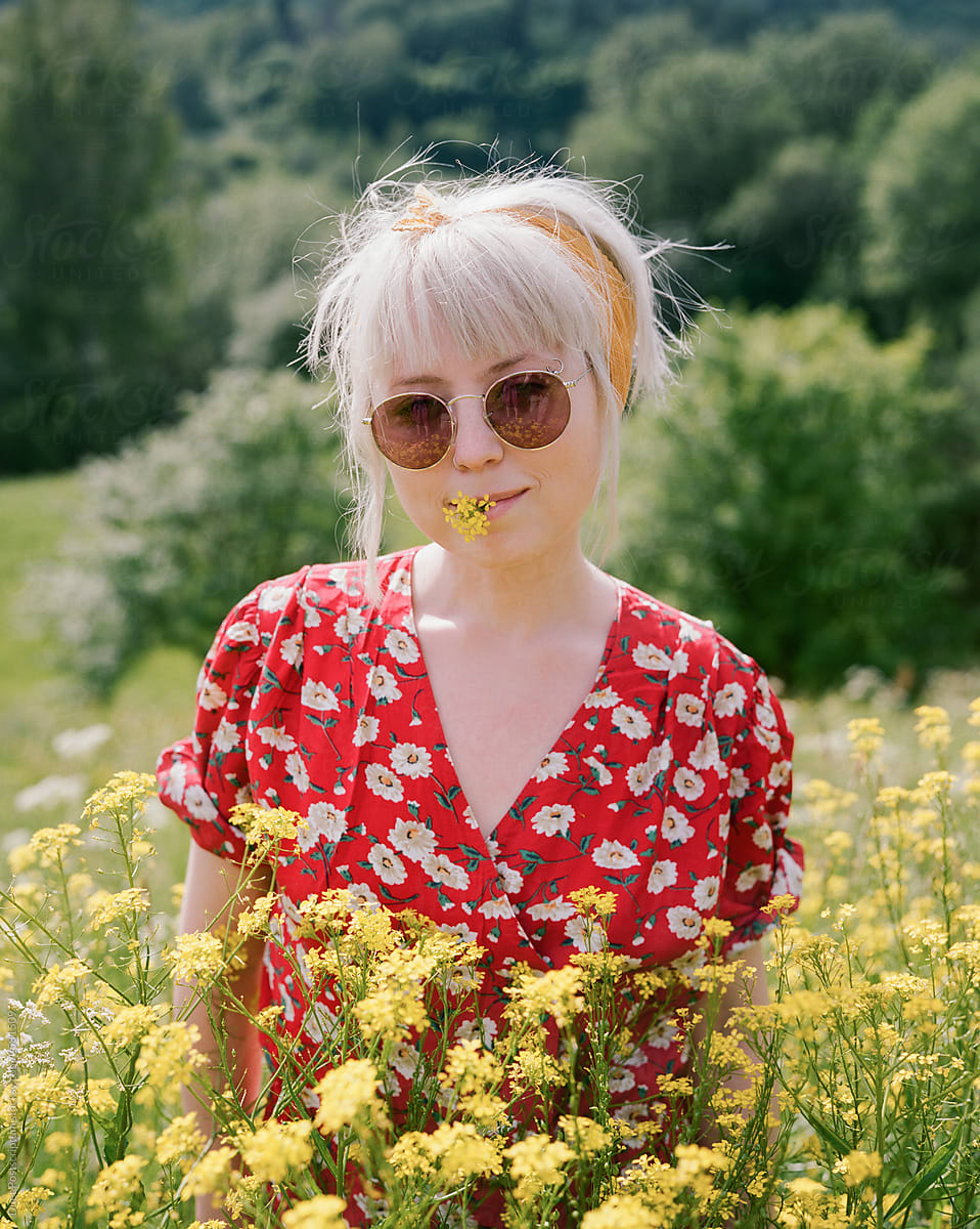 Pretty young woman in field with yellow flowers in her mouth