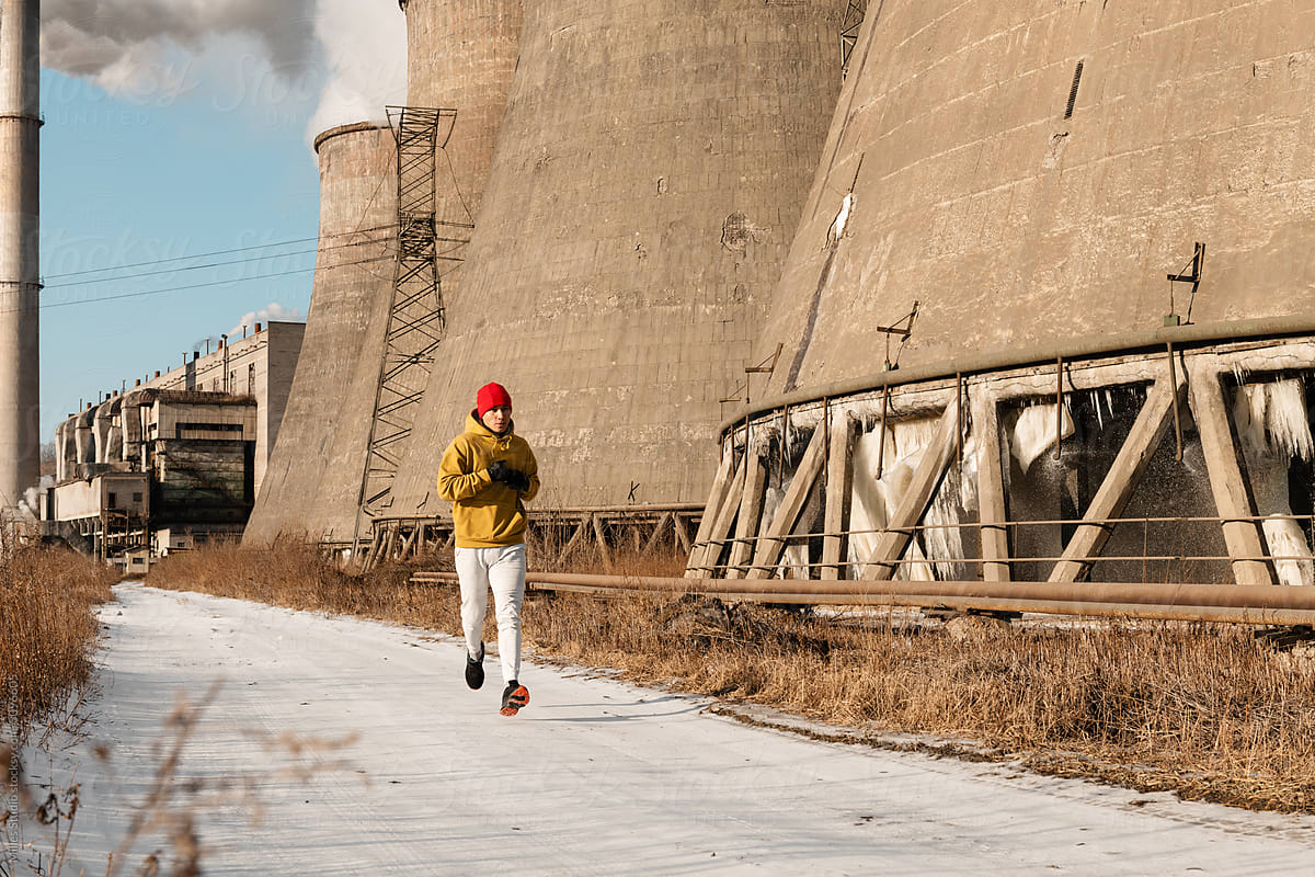 Sportsman running near grungy factory pipes on winter day
