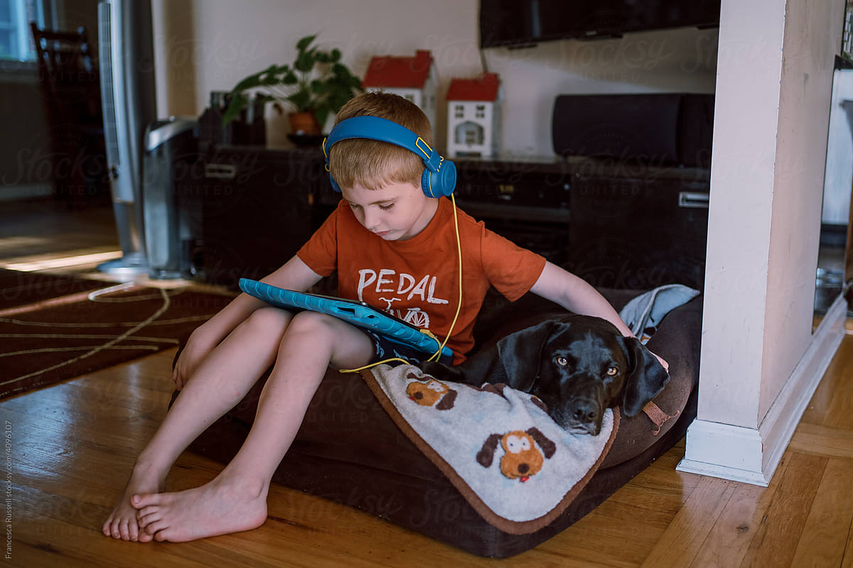 A little boy sits in a dog bed with his dog.