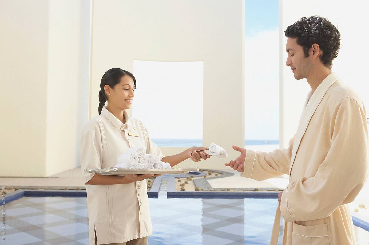 Hotel service employee giving a towel to guest at spa