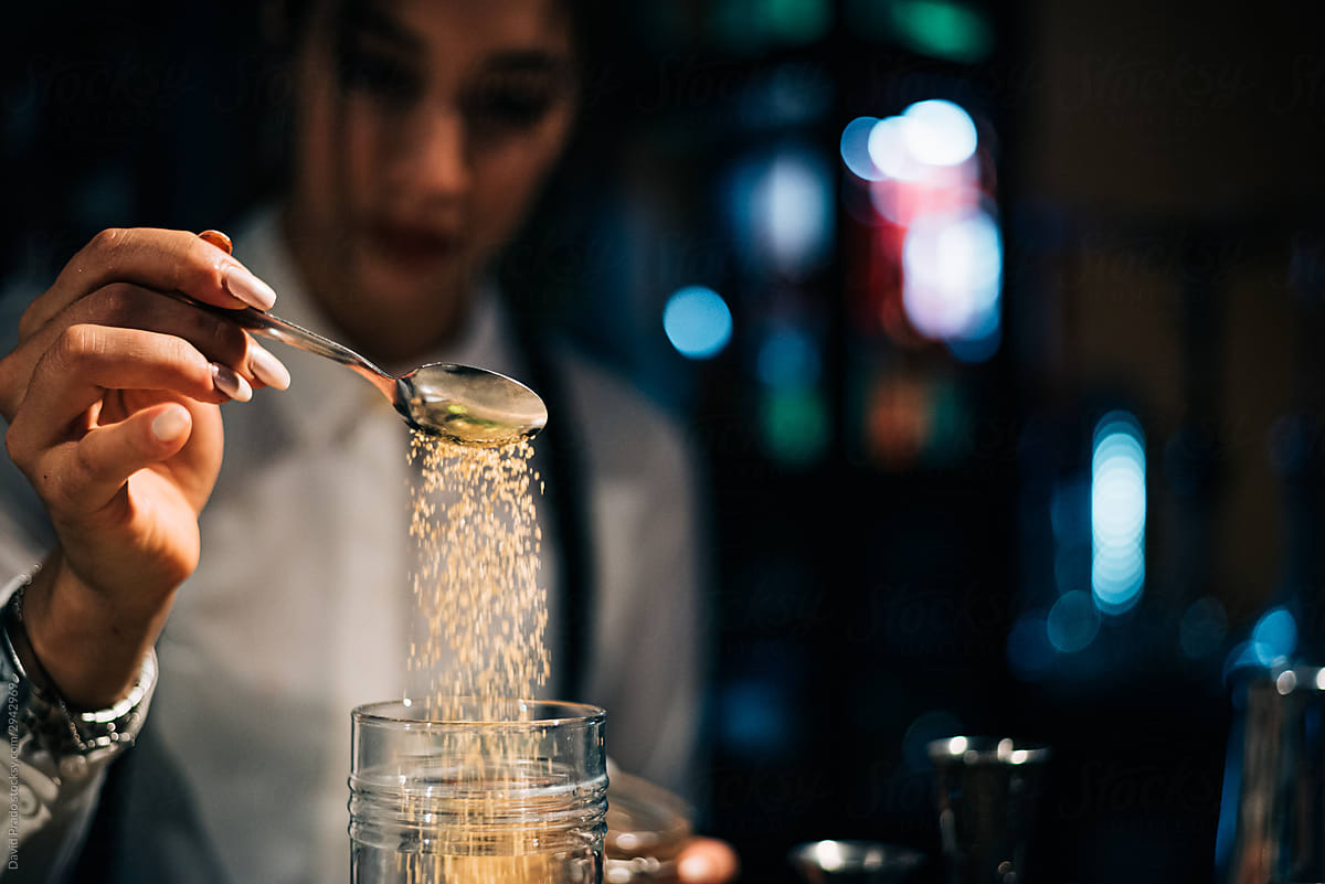 Crop bartender adding ingredient in cup