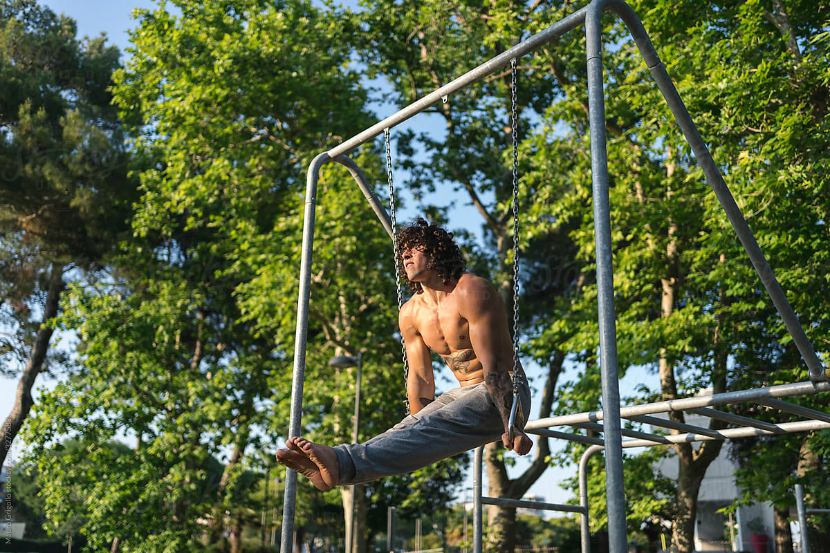 Fit man doing pull-ups at the rings in a park